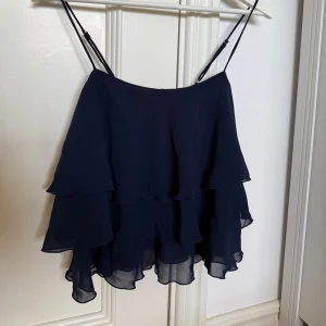 Mörkblå volangtopp från Gina Tricot - Säljer en mörkblå volangtopp från Gina Tricot med tunna axelband och flera lager volanger. Endast använd några få gånger och i mycket bra skick!