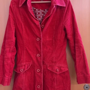 Röd manchesterkappa från H&M L.O.G.G. - Säljer en röd manchesterkappa från H&M L.O.G.G. i storlek 40. Jackan har långa ärmar, knappar framtill och två fickor med lock. Snygg krage och dekorativt bälte bak. Perfekt för dig som gillar färg och retrostil!