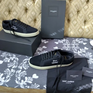 Svarta sneakers från Saint Laurent - Säljer ett par svarta Saint Laurent sneakers med beige sula och svart top. Skorna har snörning och är tillverkade i canvas och skinn. Perfekta för dig som gillar stilrena och exklusiva sneakers.