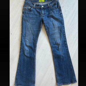 Blå bootcut jeans från Strut - Säljer ett par klassiska blå bootcut jeans från Sweet med fickor och snygga detaljer på bakfickorna. Jeansen har normal passform och stängs med dragkedja och knapp.
