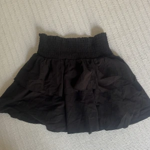 Svart volangkjol från SHEIN - Supersöt svart kortkjol från SHEIN med volanger och smock i midjan. Kjolen är i en lätt och luftig modell som passar perfekt till sommaren. Enkel att matcha med olika toppar för en trendig look.