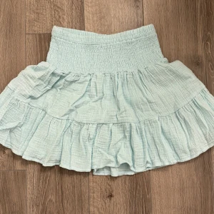 Ljusblå volangkjol - Supersöt ljusblå kjol med bred resår i midjan och volangdetaljer. Kjolen är kort och har en luftig känsla, perfekt för varma dagar. Passar dig som gillar en feminin och avslappnad stil.