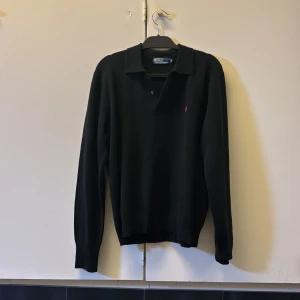 Svart pikétröja från Polo Ralph Lauren - Klassisk svart pikétröja med lång ärm från Polo Ralph Lauren. Tröjan har krage, knäppning vid halsen och den ikoniska röda loggan broderad på bröstet. Perfekt för en stilren och avslappnad look. Nypris runt 2900, mitt pris 699! Koftan/ tröjan är knappt använd och är i princip som nyskick. Pris går att diskuteras! Hör av er vid minsta lilla fundering🤗