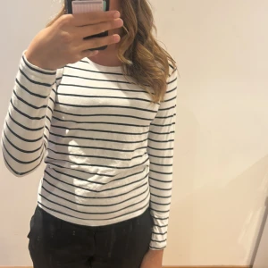 Vit och svart randig långärmad tröja från Basic You - Säljer en vit långärmad tröja med svarta horisontella ränder från Basic You. Tröjan är tillverkad i ekologisk bomull och har en klassisk, normal passform. Perfekt för en enkel och stilren look.