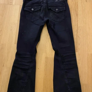 Svarta bootcut jeans från True Religion - Säljer ett par svarta bootcut jeans från True Religion med klassiska fickor med lock och knapp bak. Jag är 175 och dom passar perfekt i längden. Dom är andvända men fortfar i bra skick.  Nypris 1200 kr. Midjemått 40 cm raktöver