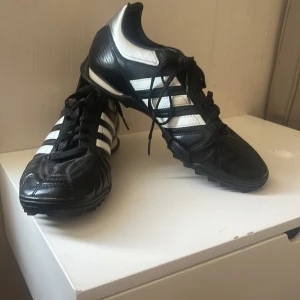  Adidas blå kvalitet - Det är Adidas för fotboll blå kvalitet fotbollsskor med vita ränder och . Skorna har rund tå och platt sula, perfekta för spel på gräs. Ikonisk design med tydlig Adidas-logga på sidan och under sulan.
