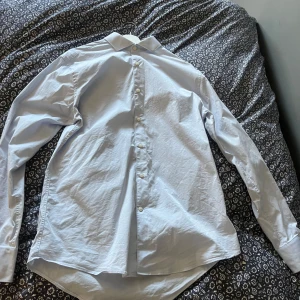 Ljusblå skjorta från tiger of sweden - Säljer en stilren ljusblå skjorta med klassisk krage och vita knappar. Skjortan har lång ärm och rak passform, perfekt till både jeans och kostymbyxor. Enkel och tidlös design som funkar till många tillfällen.