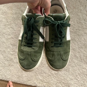 Valentino sneakers i grönt och vitt mocka - Säljer ett par snygga Valentino sneakers i grön mocka med vita detaljer och coola nitar på hälen. Skorna har snörning och rund tå, samt en platt sula. Perfekta för dig som vill sticka ut med stilrena men unika sneakers. Skick 7/10 lote hältramp och en nit är av. (Pris kan diskuteras)