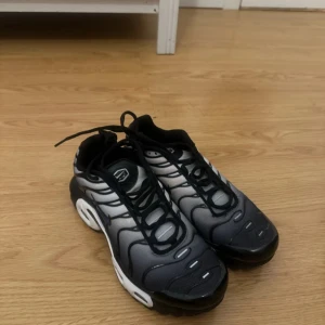 Nike Air Max Plus Tn sneakers svart och grå - Nike Air Max Plus Tn sneakers i svart och grå med vita detaljer. Skorna har klassisk snörning, synlig Tn-logo bak och på sulan, samt vågformade linjer på ovandelen . Äkta! 