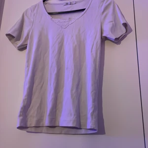 Vit blus med spets från Flash - Säljer en söt vit blus från Flash med korta ärmar och v-ringning. Vid halsen finns en fin spetsdetalj som ger en extra touch. Perfekt att styla med jeans eller kjol för en fräsch look.