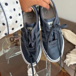 Mörkblå Adidas sneakers strl 38 - Klassisk Adidas, sambas - liknande skor. Ränder i mocka på sidan och vit sula. Har klistrat på sånt skydd bak vid hälen för att jag alltid får skoskav (kan tas bort men rätt najs att ha). Kommer inte till användning tyvärr!