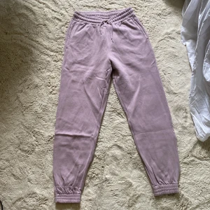 Ljuslila mjukisbyxor från Kappahl - Mysiga ljuslila mjukisbyxor från Kappahl med resår och snörning i midjan. Byxorna har muddar vid bensluten och praktiska sidofickor. Perfekta för chill dagar eller när du vill vara extra bekväm.