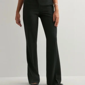 Svarta kostymbyxor från Nelly - Säljer ett par lågmidjade svarta kostymbyxor från Nelly med klassisk rak passform och diskreta fickor. Byxorna har hällor för bälte och stängs med dragkedja och knappar. Perfekta för en clean och stilren look.