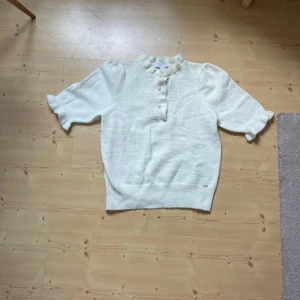 Vit stickad blus med puffärm - Supersöt vit stickad blus från Lindex med korta puffärmar, volangkrage och knappar framtill. Mjuk och skön, passar till både jeans och kjol.