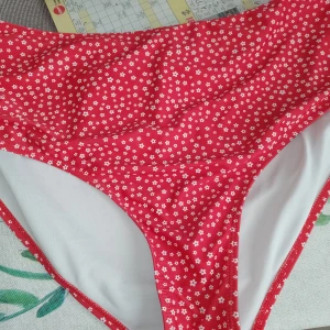 Röd blommig bikini med hög midja - Superfin bikini i rött med små vita blommor över hela tyget. Underdelen har hög midja och klassisk bikini-trosa form. Perfekt för strandhäng och poolparty! Materialet känns mjukt och följsamt mot huden.