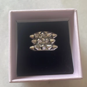 Edblad ring i storlek S 16.80 - Cool och edgy silvrig ring med flera konformade nitar och rundade detaljer. Perfekt accessoar för dig som vill sticka ut och ge din look en tuffare vibe. Ringen är bred och har en unik design som drar blickarna till sig.