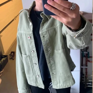 Ljusgrön jeansjacka med knappar - Snygg ljusgrön jeansjacka med klassisk rak passform och stora fickor framtill. Jackan har silvriga knappar och är långärmad, perfekt att slänga över en hoodie eller t-shirt. Enkel och stilren design som funkar till det mesta.