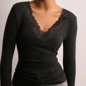 Svart långärmad topp med spets - Supersnygg svart långärmad topp med djup v-ringning och bred spetskant runt halsen. Figurnära passform som framhäver siluetten och ger en elegant vibe. Perfekt att styla med jeans eller kjol för en trendig look.