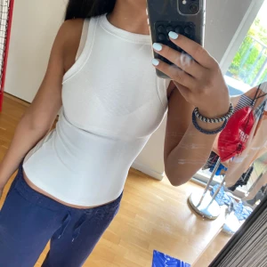 Vit ribbad linnetopp - Säljer en fräsch vit ribbad linnetopp med tight passform och ärmlös design. Perfekt för varma dagar eller att styla lager på lager. Enkel och stilren med rund halsringning och stretchigt material som sitter snyggt på kroppen.