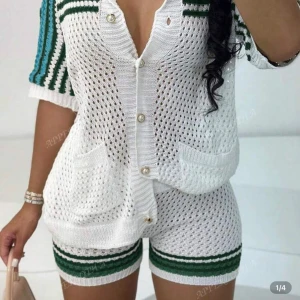 Vita kortärmad stickad T-shirt med matchande shorts  - Snygga vita stickade shorta med matchande shorts med gröna och mörkgröna ränder längst ner . De är virkade med hålmönster och har en bekväm, normal passform. Perfekta för sommarens varma dagar och ger en sportig, trendig vibe.