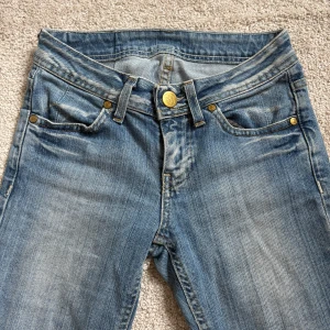 Ljusblå low waist jeans - Säljer ett parjeans i ljusblå tvätt. Jeansen har raka ben, låg midja och snygga slitningar framtill. Guldiga nitar och knappstängning ger en tidlös look. Perfekta till sneakers eller boots. Storlek 25/32, jag är ca 157cm💓