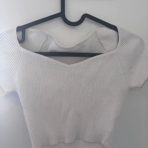 Vit ribbad croppad topp - Säljer en vit ribbad croppad topp med korta ärmar och v-ringad hals. Toppen har en tight passform och är perfekt för dig som gillar en enkel men snygg stil. Superfin att matcha med jeans eller kjol!
