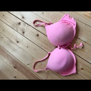 Rosa ribbad bikiniöverdel 85E - Supersöt rosa bikiniöverdel från Censored i storlek 85E. Den har ribbad struktur, vadderade kupor och snygg snörning framtill. Justerbara axelband för perfekt passform. Perfekt för strandhäng eller poolparty!