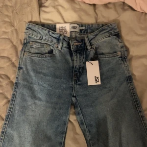 Bootcut jeans 90's från lager 157, ljusblå - Säljer ett par ljusblå bootcut jeans från 157 i storlek XXS. Modellen är inspirerad av 90-talet med full längd och klassiska fickor bak med lock och knappar. Jeansen har låg midja och är tillverkade i bomull för en skön och avslappnad känsla. Köptes helt nya på rea för 200kr men säljs nu för 100kr
