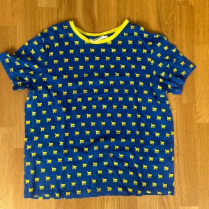 Ullared T-shirt  - Blå t-shirt från Ullared med korta ärmar och coolt mönster av små gula får över hela tröjan. Kragen är gul och ger en extra poppig kontrast. Perfekt för dig som gillar färg och roliga prints.