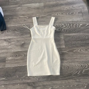 Vit kort klänning från Amisu - Supersnygg vit kort klänning från Amisu med breda axelband och en liten slits framtill. Klänningen har en figurnära passform och är gjord i ett mjukt, lätt material som känns bekvämt mot huden. Perfekt för dig som gillar en clean och stilren look.