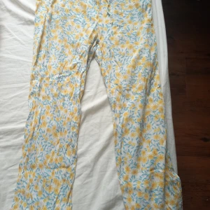 Blommiga linnebyxor med snörning - Lätta och luftiga linnebyxor med blommigt mönster i gult och blått på vit botten. Byxorna har resår och snörning i midjan för skön passform. Perfekta för varma dagar och chill vibes.