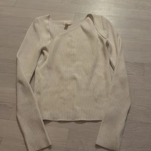 Vit ribbad långärmad tröja - Säljer en vit ribbad tröja med lång ärm och snygg asymmetrisk halsringning. Tröjan är i mjukt material och har en stilren look som passar perfekt till jeans eller kjol. Enkel att matcha och superbekväm för alla tillfällen.