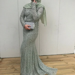Glittrig festklänning - Supersnygg ljusgrön långklänning med glittriga paljetter över hela klänningen. Den har lång ärm, figurnära passform och en elegant, svepande kjol. Perfekt för bal eller fest där du vill sticka ut och glänsa. Klänningen är endast använd två gånger och därefter kemtvättad. 