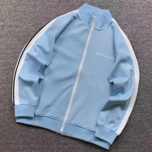 Palm Angels kofta (blå) - Snygg ljusblå track jacket från Palm Angels med vita ränder längs ärmarna och vit dragkedja framtill. Jackan har hög krage och ribbade muddar. Perfekt för en sportig och trendig look.