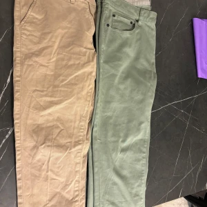 Beiga och gröna chinos i bomull - Två par chinos i snygga färger från Dressman – ett par i beige och ett i dämpad grön. Båda har raka ben, klassiska fickor och är tillverkade i mjuk bomull. Perfekta för en clean och avslappnad look. Passar dig som gillar stilrena och enkla byxor.