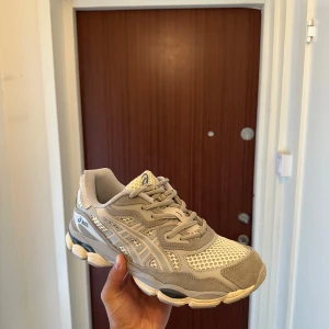 Beige och vita Asics sneakers - Snygga Asics sneakers i beige och vitt med meshpaneler och detaljer i mocka. Skorna har rund tå, snörning och en chunky sula som ger en sportig vibe. Perfekta för dig som gillar stilrena och bekväma sneakers med retroinspirerad look.