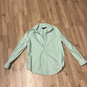 Ljusgrön skjorta från Polo Ralph Lauren - Snygg ljusgrön skjorta från Polo Ralph Lauren i relaxed fit. Skjortan har klassisk krage, långa ärmar och knäppning framtill. Tillverkad i mjuk bomull och pryds av den ikoniska broderade loggan på bröstet. Perfekt för en clean och stilren look.