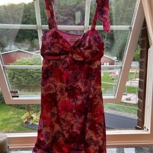 Blommig miniklänning från Adoore - Supersöt miniklänning från Adoore med blommigt mönster i lila, rosa och rött. Klänningen har breda axelband, rosett-detalj framtill och en feminin passform. Perfekt för sommarens alla tillfällen! Köpt på adoores samplesale och oanvänd med lappen kvar!