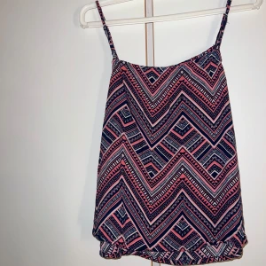 Mönstrad linnetopp i rosa och marinblå - Säljer en snygg linnetopp med tunna axelband och grafiskt mönster i rosa, marinblått och vitt. Toppen är tillverkad i 100% viskos och har en luftig passform, perfekt för varma dagar. Mönstret är riktigt iögonfallande och ger en cool vibe. Lappen för storleken finns inte kvar men jag vet att det är storlek xs