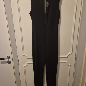 Svart byxdress från NLY One, stl M - Säljer en svart ärmlös byxdress från NLY One i storlek M. Byxdressen har djup v-ringning fram och smal passform i benen. Perfekt för dig som gillar stilrena och enkla plagg med en snygg siluett.