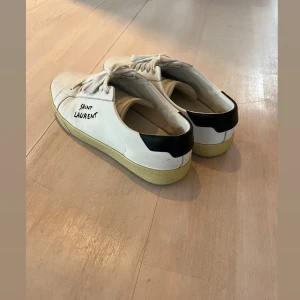 Saint Laurent vita sneakers med svart detalj - Snygga vita sneakers från Saint Laurent. Kör en intresse koll, så läng iväg ett bud priset är diskuerbart! Går nog att snygga till lite då de är relativt sparsamt använda. Alla tillbehör och låda finns kvar sedan köp! 