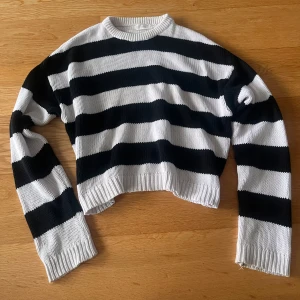 Randig svartvit stickad tröja - Säljer en stickad tröja med breda svarta och vita ränder. Tröjan har en croppad passform, rund halsringning och långa ärmar med ribbade muddar. Perfekt för dig som gillar en chill och trendig stil. Använd fåtal gånger och har bra skick, normal i storlk.