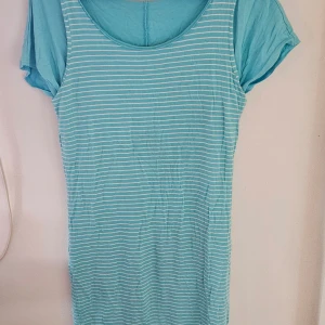 Turkos randig kortklänning från Rainbow - Supersöt turkos kortklänning från Rainbow med vita horisontella ränder. Klänningen har rund halsringning och korta ärmar. Tillverkad i mjuk bomull, perfekt för varma dagar. Enkel och fräsch stil som är lätt att matcha med sneakers eller sandaler.