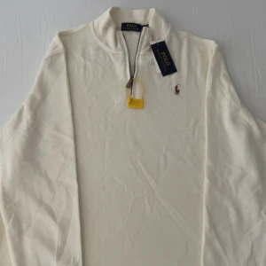 Beige RL Half Zip - Helt ny Polo Ralph Lauren Half Zip. Aldrig använt innan. Tillkommer med original förpackning och har även prislappen kvar. Perfekt fynd nu när skolan snart börjar och du behöver en ny clean outfit. Öppen för offer!