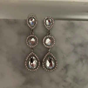 Glittriga silverfärgade örhängen - Festliga örhängen i silverfärg med stora droppformade och runda stenar som är omgivna av små gnistrande stenar.