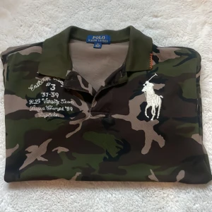 Camouflage pikétröja från Ralph Lauren - Snygg pikétröja från Polo Ralph Lauren i camouflage-mönster med broderad vit logga på bröstet. Klassisk krage, korta ärmar och coola broderade detaljer framtill. Perfekt för dig som vill sticka ut med streetstyle-vibe.