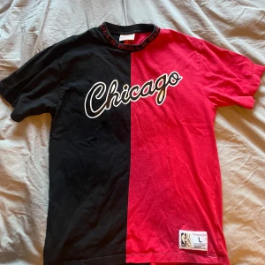Chicago Bulls t-shirt Mitchell & Ness - Snygg Chicago Bulls t-shirt från Mitchell & Ness i storlek L. T-shirten är delad i svart och röd med 'Chicago' tryckt på bröstet och BULLS-detaljer runt kragen. Tillverkad i mjuk bomull och har klassisk passform 