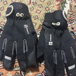 Svarta handskar från Balance - Säljer ett par svarta handskar från Balance med grå detaljer. De har justerbara remmar vid handleden och är perfekta för kyligare väder. Handskarna har en stilren design med små logotyper och är bekväma att bära.