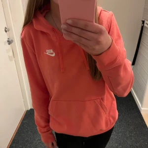 Corall hoodie från Nike - Säljer en snygg corall färgad hoodie från Nike med klassisk logga på bröstet. Tröjan har en stor ficka framtill och justerbar huva med dragsko. Perfekt för en avslappnad stil. Nästintill oanvänd och i väldigt bra skick💕