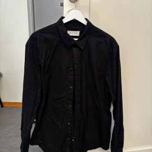 Svart skjorta - Snygg svart skjorta från Pier One med klassisk krage och knappar framtill. Perfekt för en stilren look.